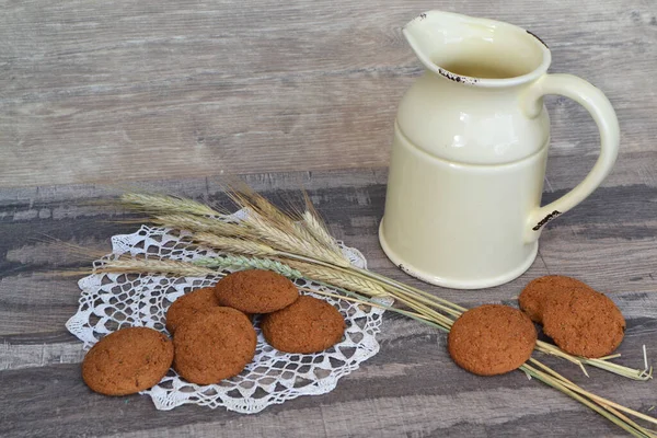 fresh crispy cereal cookies and ears on rustic wooden table with mug of milk and knitted white napkin