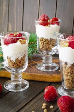 Kremalı, müsli ve koyu ahşap masada taze çilek soslu sağlıklı katmanlı tatlı.
