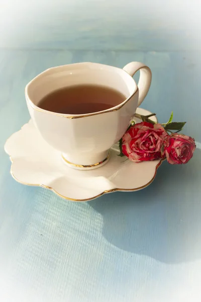 White cup of tea and roses on blue background, vintage