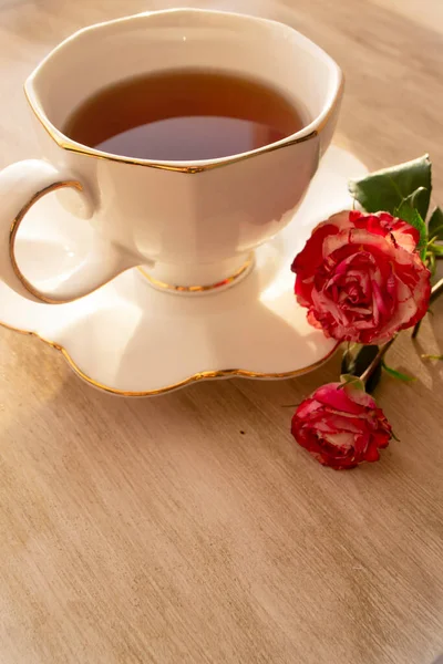 Cup of tea in a china cup and saucer, on a distressed table and roses