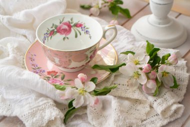 Pembe, klasik çay partisi, çay fincanı ve ahşap tepside yumuşak çiçekler ve dantelli masa örtüsü.