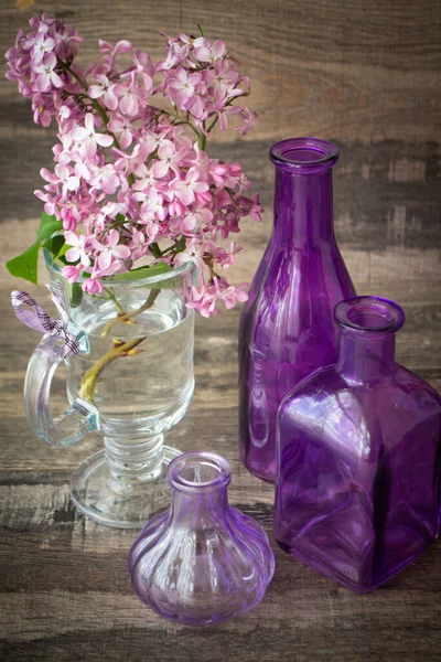 branch of blooming lilac in a glass bottle with violet bottles decoration, vertical image