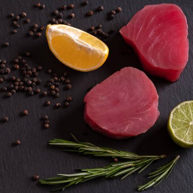 Biftek için taze çiğ ton balığı fileto, limon tuzlu biber ve koyu siyah kırsal arka planda baharatlar. Lezzetli balık yemeği. Yemek pişirmek için gerekli malzemeler