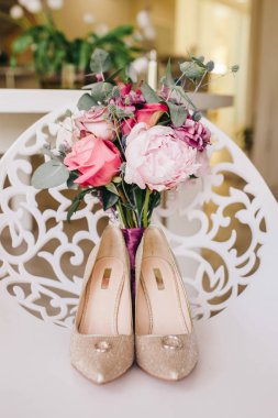 Alyans ve çiçeklerle evde beyaz bir sandalye üzerinde yüksek topuklar üzerinde zarif Altın Ayakkabı