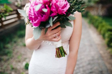 Yüzük elinde bir buket pembe peonies duran bir parkta tutan gelin