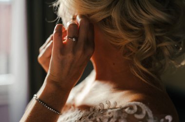 Sarışın gelin küpeleri takıyor, gelinin elinde de taşlı bir nişan yüzüğü ve bileziği var.