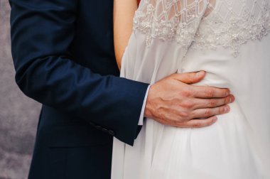 Mavi takım elbiseli damat beyaz gelinlikli geline sarılıyor.