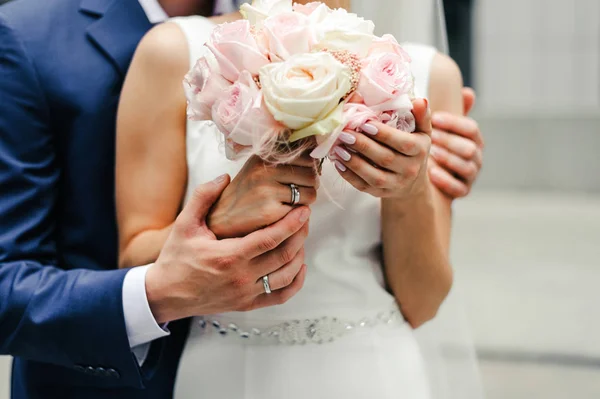 新娘手持一束粉色和白色的玫瑰 手上拿着羽毛 新郎则在背景上亲吻新娘 — 图库照片