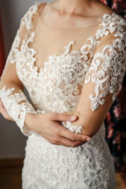 Güzel bir dantel elbise giymiş ve beline sarılmış bir gelinin elleri.