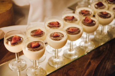 Çikolatayla kaplı sütlü tatlılar ve bardakla servis edilen çilekler bir masanın üzerinde.