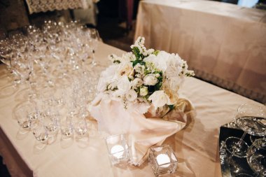 Masa örtüsüyle süslenmiş. Masada çiçekler, mumlar ve boş bardaklar var.