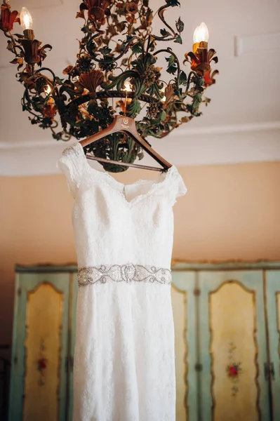 Tasarımcı avizesine asılı taşlarla işlenmiş kemerli beyaz dantelli gelinlik.