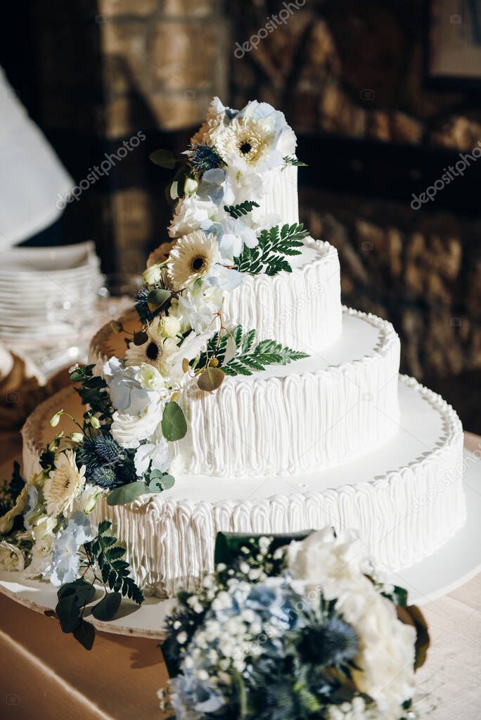 White wedding four tier cake decorated with fresh flowers and greenery