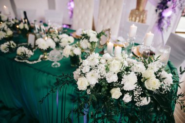 Beyaz çiçeklerin süslemesi, yeşillik, mumlar yeşil bir bezle şenlik masasında.