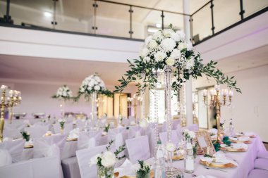 Düğün ziyafeti alanındaki şenlik masasında çiçekler, mumlar, tabaklar, çatal bıçak takımı, peçeteler var. 