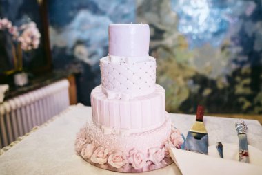 Masanın üzerinde yumuşak pembe mastikle süslenmiş üç katlı düğün pastası.