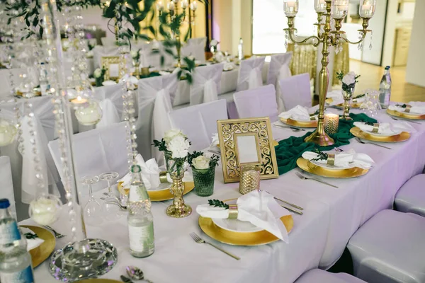 結婚式の宴会エリアには緑のテーブルクロスのテーブルがあり テーブルの上には花と緑 キャンドル カトラリー プレートの上にナプキンがあり シャンパンの2本があります — ストック写真