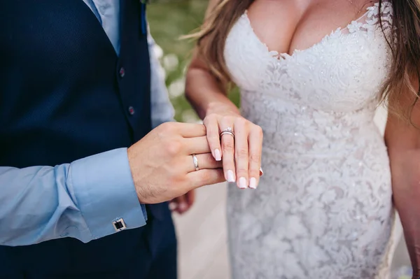 新娘穿着白色婚纱 新郎穿着西服 站在婚礼拱门旁边 把一枚戒指戴在新娘的手指上 戴在水的背景上 — 图库照片