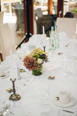 Misafirler için düğün masası, masanın üzerinde bir masa örtüsü, çiçekli vazolar, mumlar, çay fincanları.