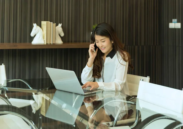Азиатская деловая женщина, использующая телефон перед ноутбуком — стоковое фото