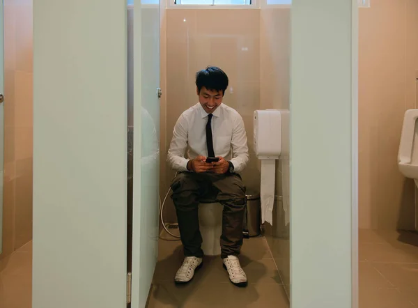Un homme d'affaires asiatique caca et en utilisant smartphone dans la salle de bain , — Photo