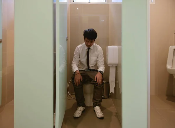 Ein asiatischer Geschäftsmann, der sich im Badezimmer wälzt, Durchfall — Stockfoto