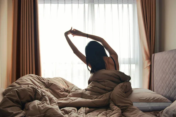 Szczęśliwa kobieta powrotem Zobacz budząc się rozciąganie w łóżku Pokój hotel — Zdjęcie stockowe