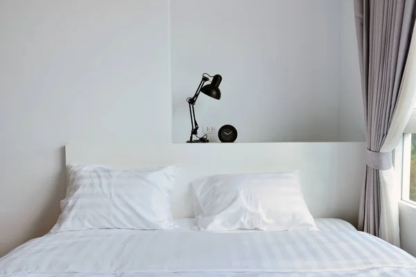 Современная лампа на деревянной тумбочке в белой современной спальне, интерьер — стоковое фото