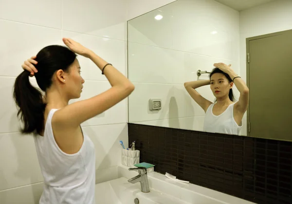 Mulher asiática escovando o cabelo na frente do espelho no banheiro — Fotografia de Stock