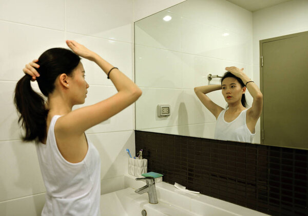 Asian woman brushing hair in front of mirror in bathroom