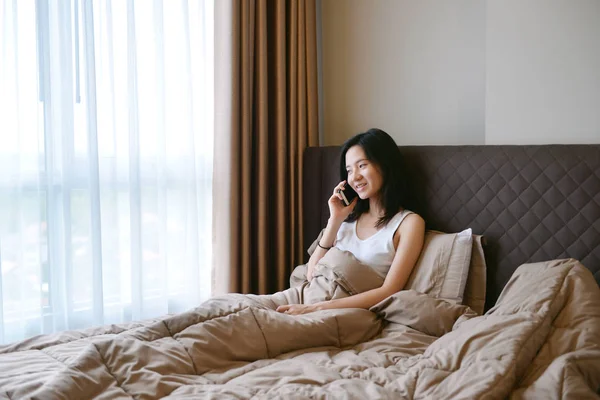 Donna asiatica sta telefonando smartphone sul letto in camera da letto di lusso — Foto Stock