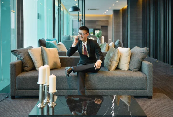 Азіатський бізнесменом за допомогою смартфона на дивані в Кондо розкішних — стокове фото