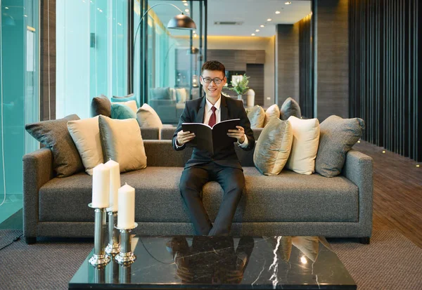 Uomo d'affari asiatico che legge un libro sul divano in condominio di lusso — Foto Stock