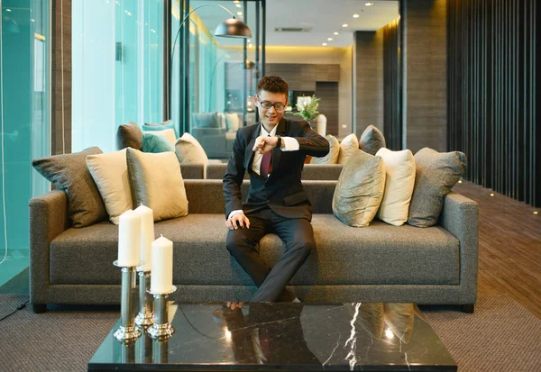 Бізнес азіатських посміхається і дивлячись на годинник на дивані в розкішні — стокове фото