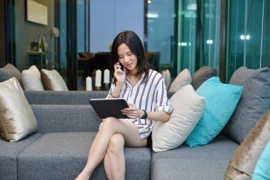 Geçici iş Asyalı telefon ederek ve tablet kanepe üzerinde kullanma kadın ben