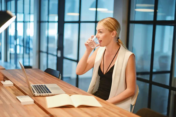 Business blonde girl drinking water in front of a laptop