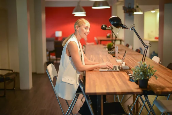 Деловая блондинка работает допоздна, использует ноутбук в офисе — стоковое фото