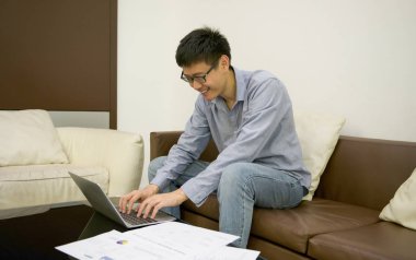 Mutlu işadamı oturma odasında belgelerle dizüstü bilgisayar kullanarak