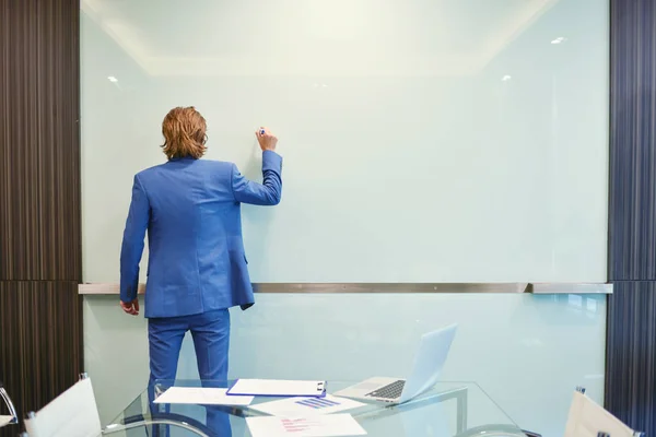 businessman back writing on blank glass board in meeting room