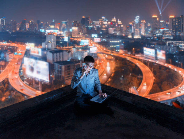 Asian man using phone and laptop with city  background, technolo