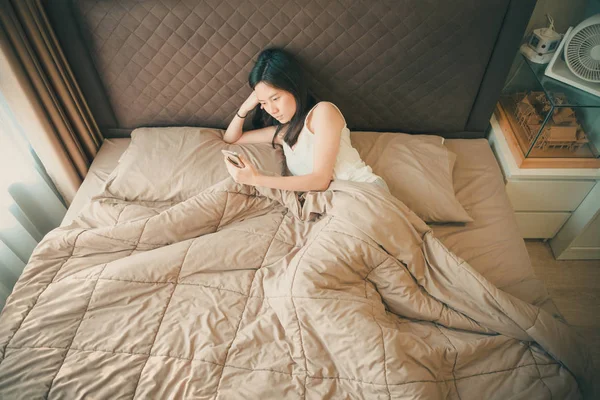 Aziatische vrouw lijdt aan depressie op bed, met behulp van een smartphone — Stockfoto