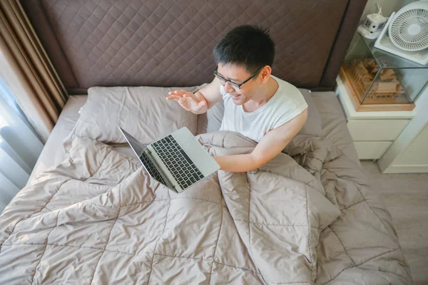 Homem asiático feliz usando um laptop na cama — Fotografia de Stock