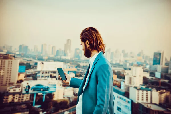 Homme d'affaires occidental utilisant un téléphone sur un toit avec une ville floue — Photo