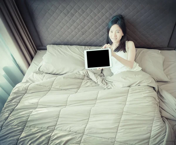 Felice donna asiatica mostrando uno schermo bianco di tablet sul letto — Foto Stock