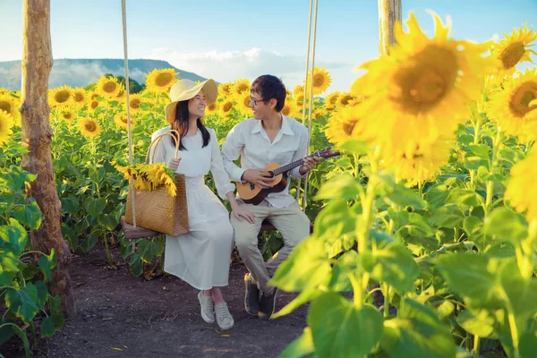 Um casal asiático desfrutando, relaxando, tocando um ukulele em sunflo — Fotografia de Stock