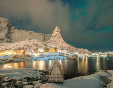 Kuzey ışıkları ve yıldızları Reine City, Lofoten adaları, Norveç, Avrupa 'da bulunan bir balıkçı köyü. Beyaz karlı dağ tepeleri ve geceleri ağaçlar, kış mevsiminde doğa manzarası.