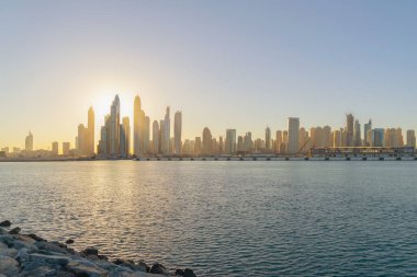 Dubai Şehir Merkezi 'nin ufuk çizgisi, deniz sahilinde dalgalar, Birleşik Arap Emirlikleri ya da BAE. Seyahat tatili konseptinde finans bölgesi. Şehir merkezi. Gökdelenler, günbatımı gökyüzü.