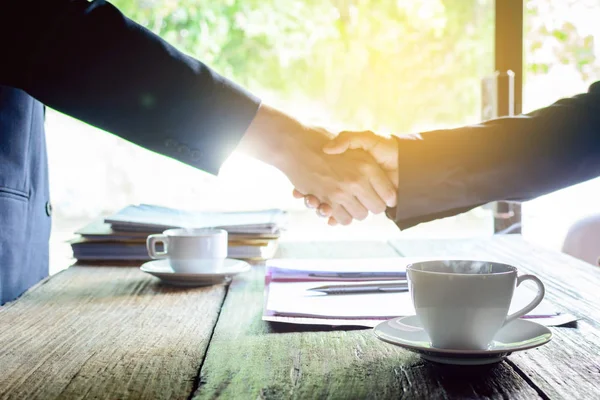 Kaffeebecher auf einem Holztisch und ein Geschäftsmann schüttelt Hände — Stockfoto