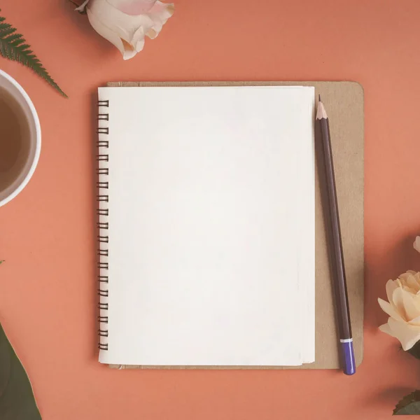 Cuaderno plano y rosa colocados en un escritorio rojo —  Fotos de Stock