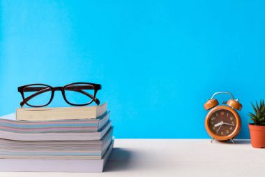 Kitaplar ve gözlük bir beyaz tahta masada saatler ve decorat vardır